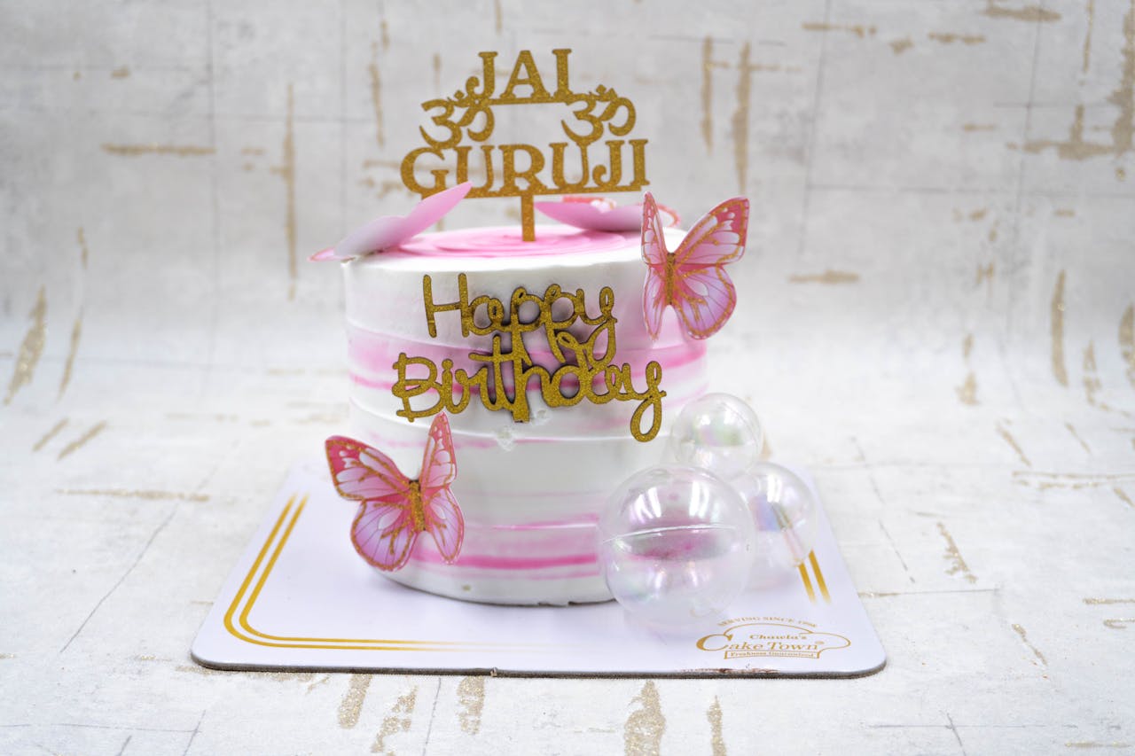 Stylish pink and white birthday cake with butterfly decorations and a Happy Birthday topper.